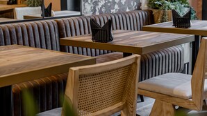 A restaurant interior with wooden tables and cushioned booths, featuring a large floral wallpaper and potted plants. - Hotel Branco Timisoara (Timisoara)
