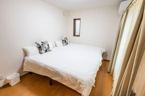 A bedroom with a large bed, white walls, a small window, and a curtain.