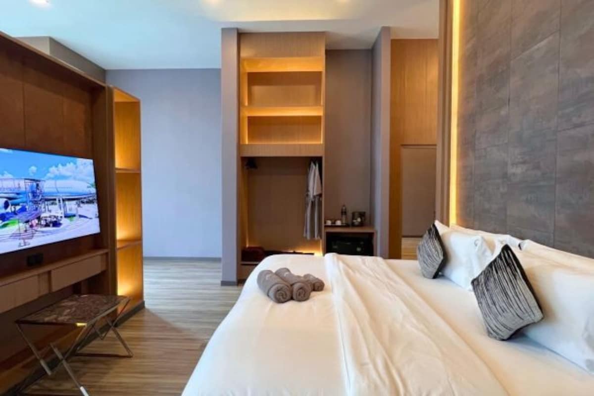 A modern hotel room with a large bed, a flat-screen TV mounted on the wall, and built-in shelving.