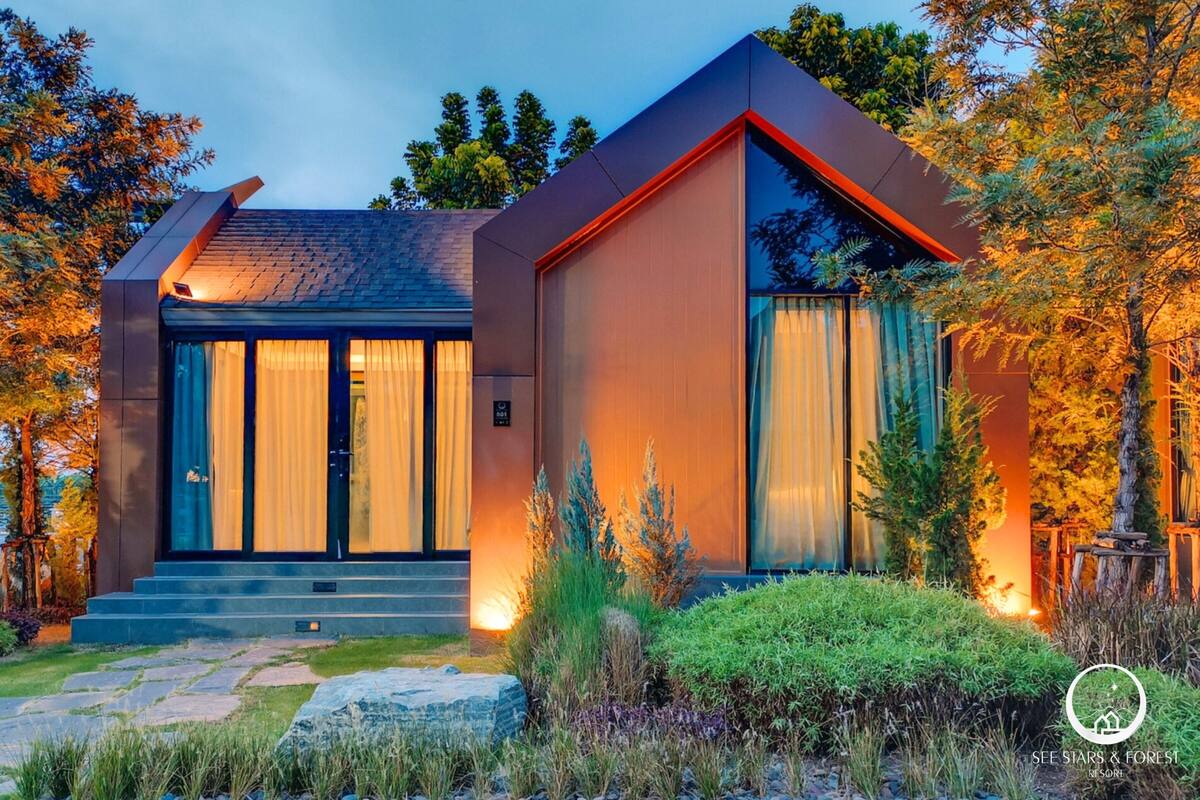 Een modern huis met twee verdiepingen, een schuin dak, grote ramen en een stenen pad dat naar de ingang leidt.