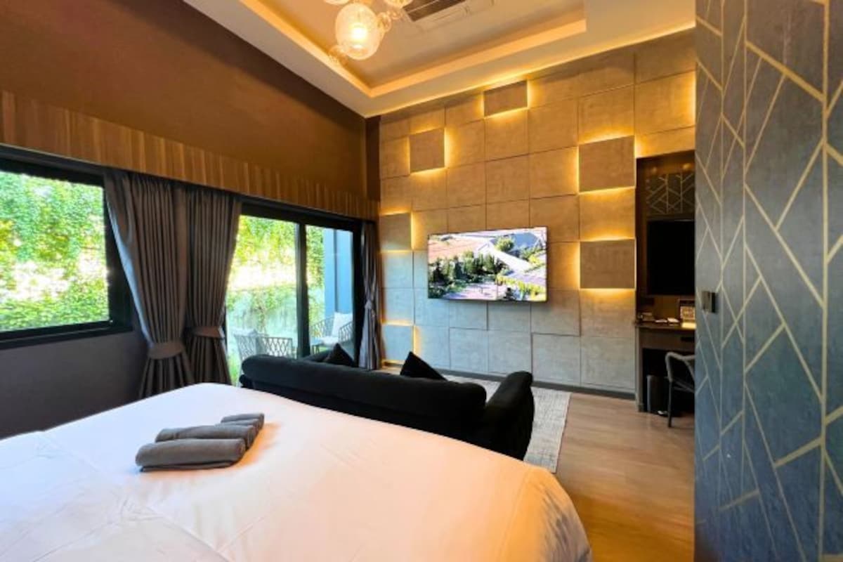 A modern hotel room with a large bed, a flat-screen TV mounted on the wall, and a seating area with a table and chairs.