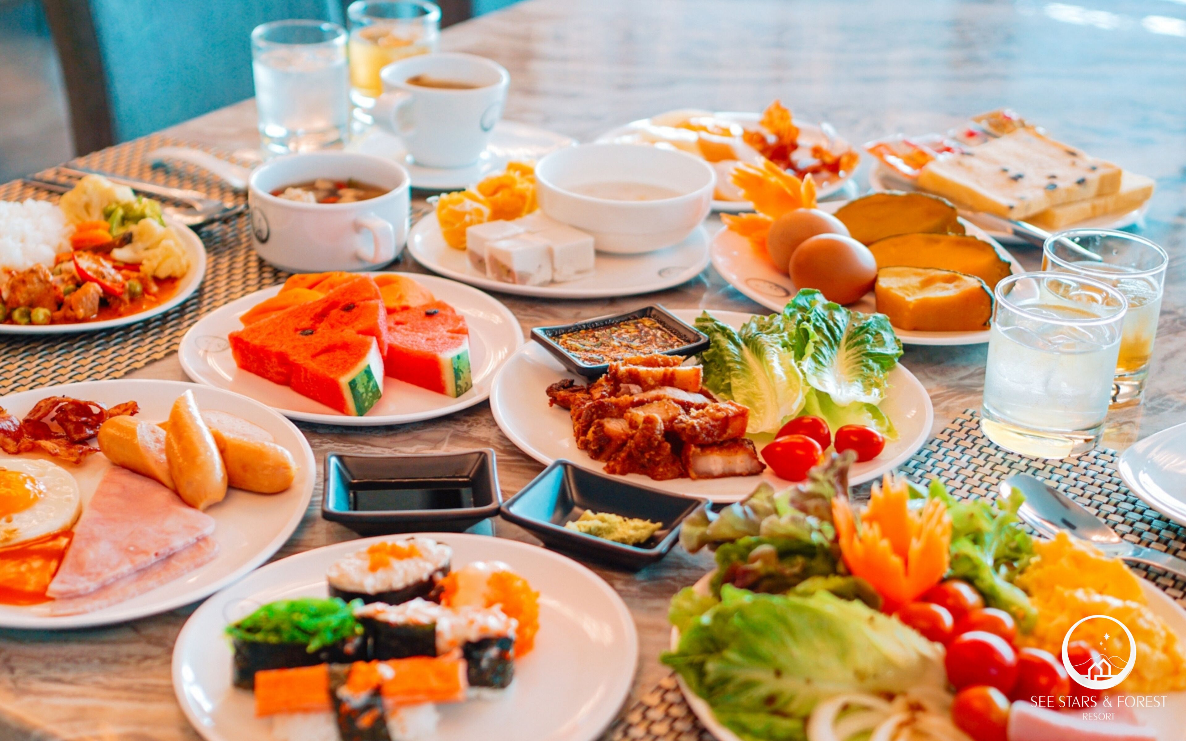 Una mesa dispuesta con diversos platos, incluyendo sushi, carne y verduras, además de vasos y copas.