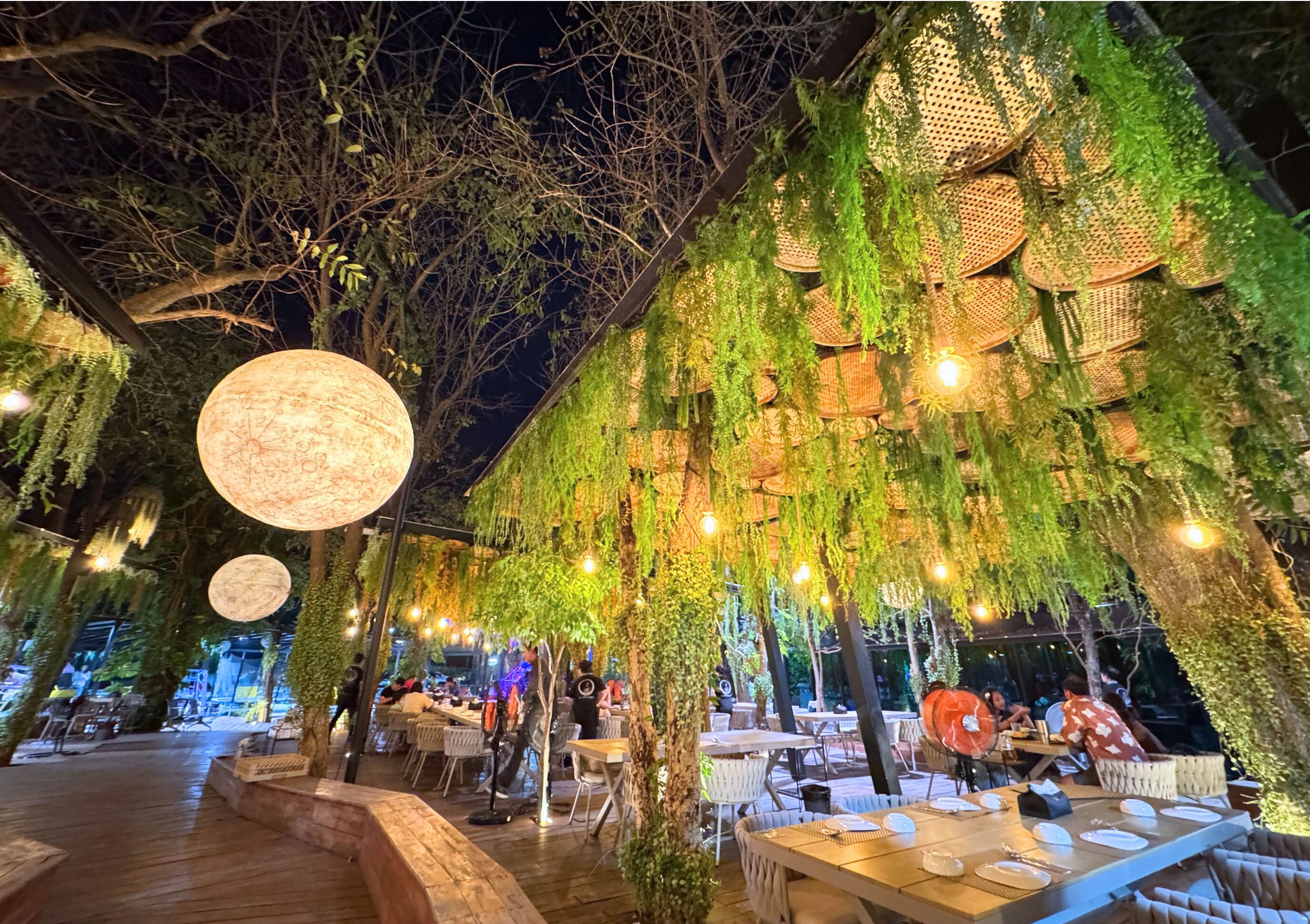 An outdoor dining area with tables and chairs, surrounded by greenery and hanging baskets.
