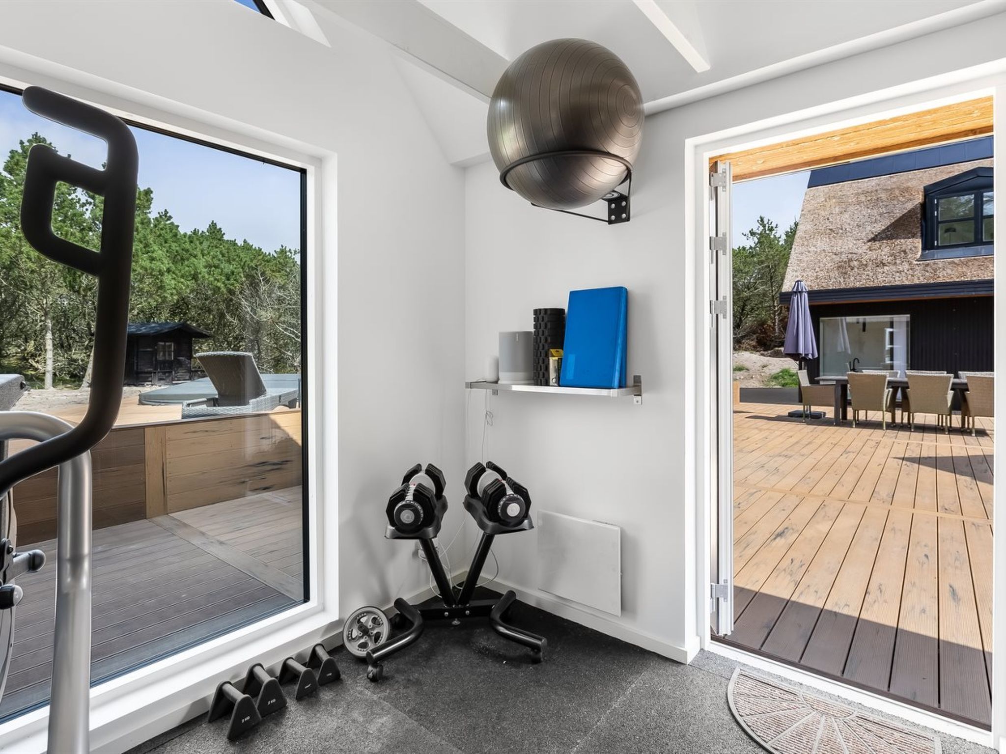Een moderne sportschool thuis met trainingsapparatuur, een groot raam en uitzicht op de achtertuin.