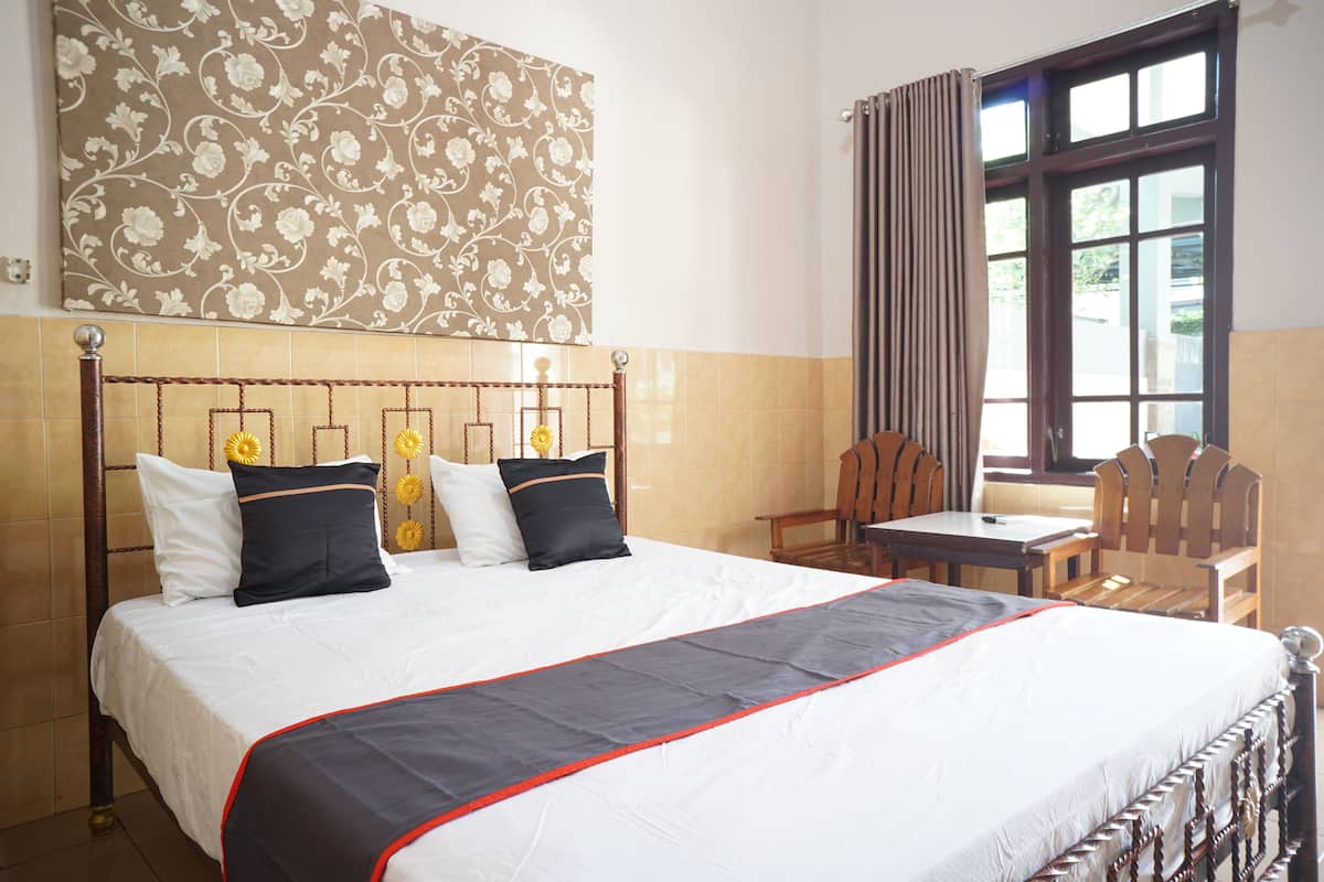 A hotel room with a large bed, a wooden headboard, a small table, and a chair.