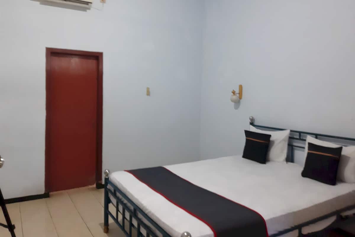 A bedroom with a single bed, a red door, and an air conditioning unit on the wall.