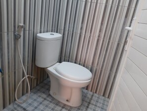 A small, compact bathroom with a toilet, a hand dryer, and a toilet paper holder. The walls are tiled with a striped pattern. - Collection O 92868 Nusantara Hotel (Banyuwangi)