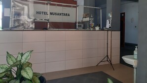 Zona de recepció d'hotel amb taulell de recepció, una planta en test, un rentaplat i un calendari a la paret.