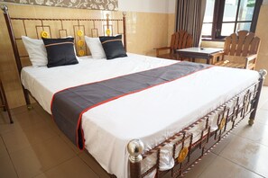 A large bed with a wooden headboard, a grey and red bedspread, and multiple pillows. There is a wooden table and chairs in the room. - Collection O 92868 Nusantara Hotel (Banyuwangi)