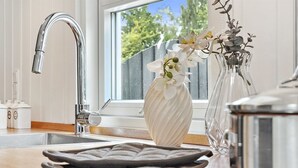 A kitchen with a stainless steel faucet, a window with a view of trees, and a vase with white flowers on the counter. - "Sylvi" - 750m from the sea by Interhome (Hals)