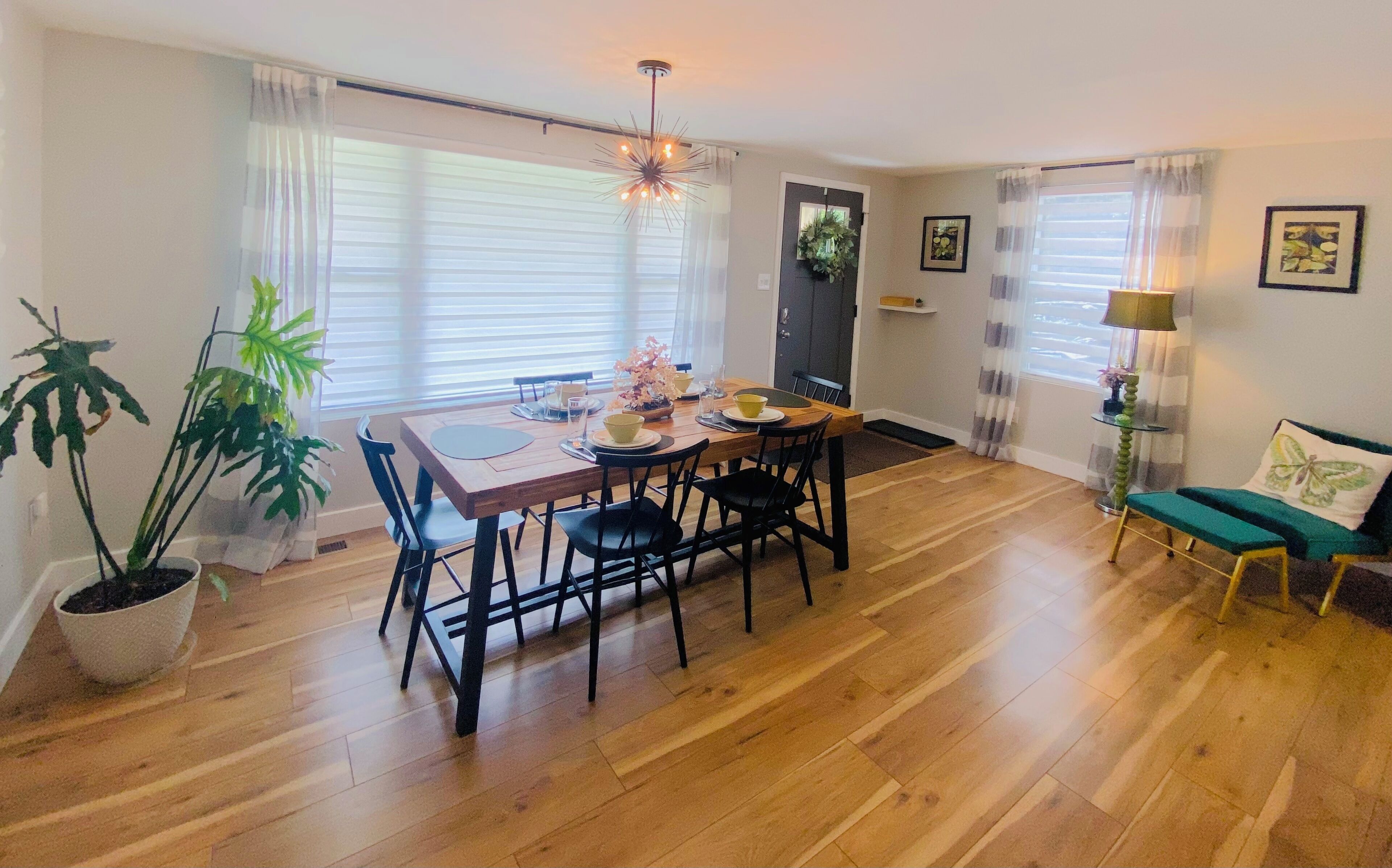 A dining area with a wooden table and chairs, a potted plant, and a door with a plant decoration.