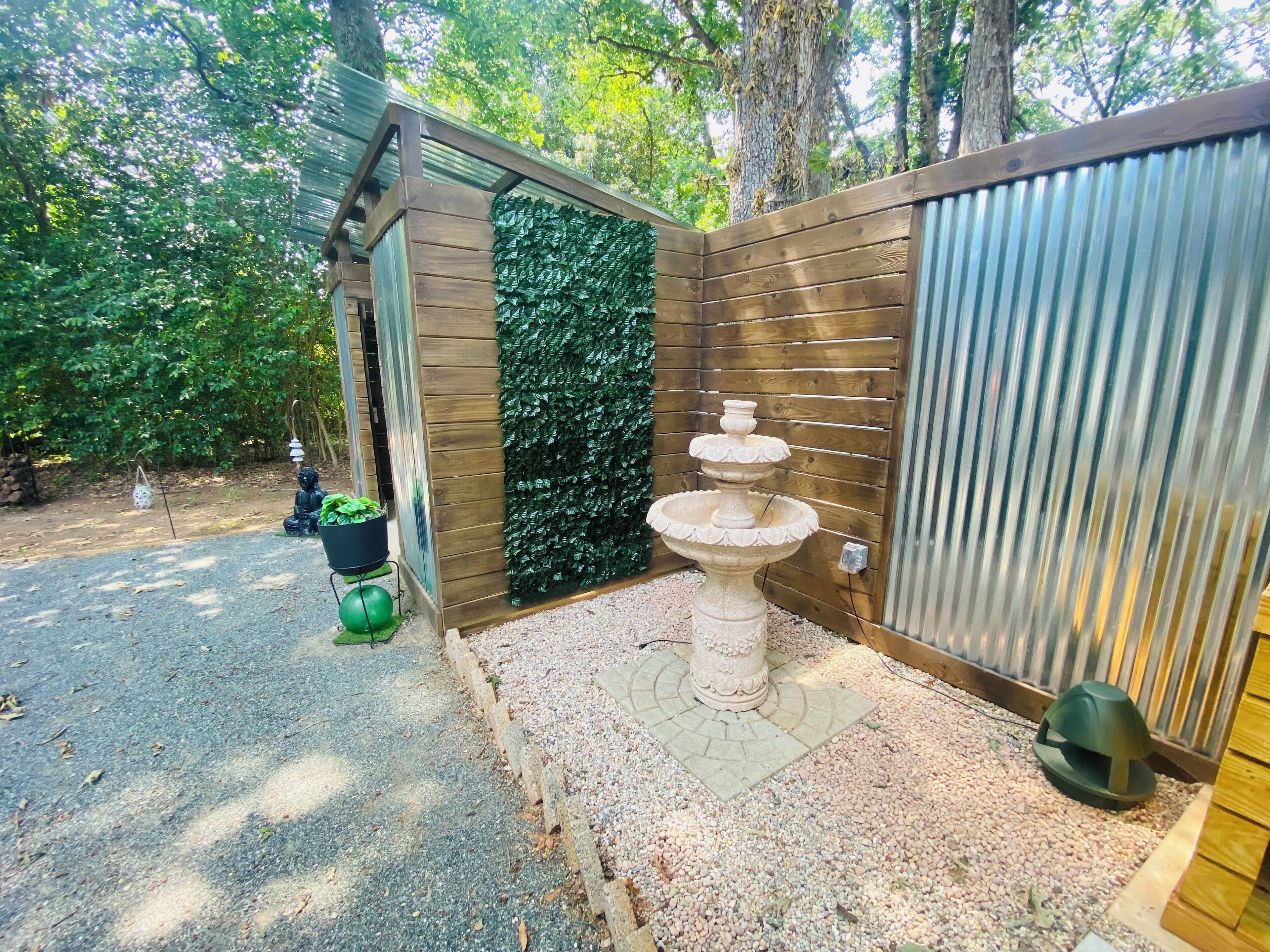 A garden area with a wooden structure, a decorative fountain, and a green wall.