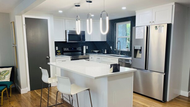 A modern kitchen with white cabinetry, stainless steel appliances, and a central island with bar stools. - 7min to Uptown - 2 Ensuites Suites w/Veranda (Charlotte)