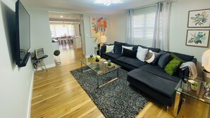 A modern living room with a black sofa, glass coffee table, and a wooden floor. - 7min to Uptown - 2 Ensuites Suites w/Veranda (Charlotte)