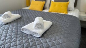Una cama bien hecha con un edredón gris acolchado y dos toallas blancas enrolladas sobre ella.