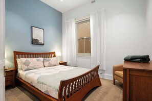 A bedroom with a wooden bed, a nightstand, a desk, and a window with curtains.
