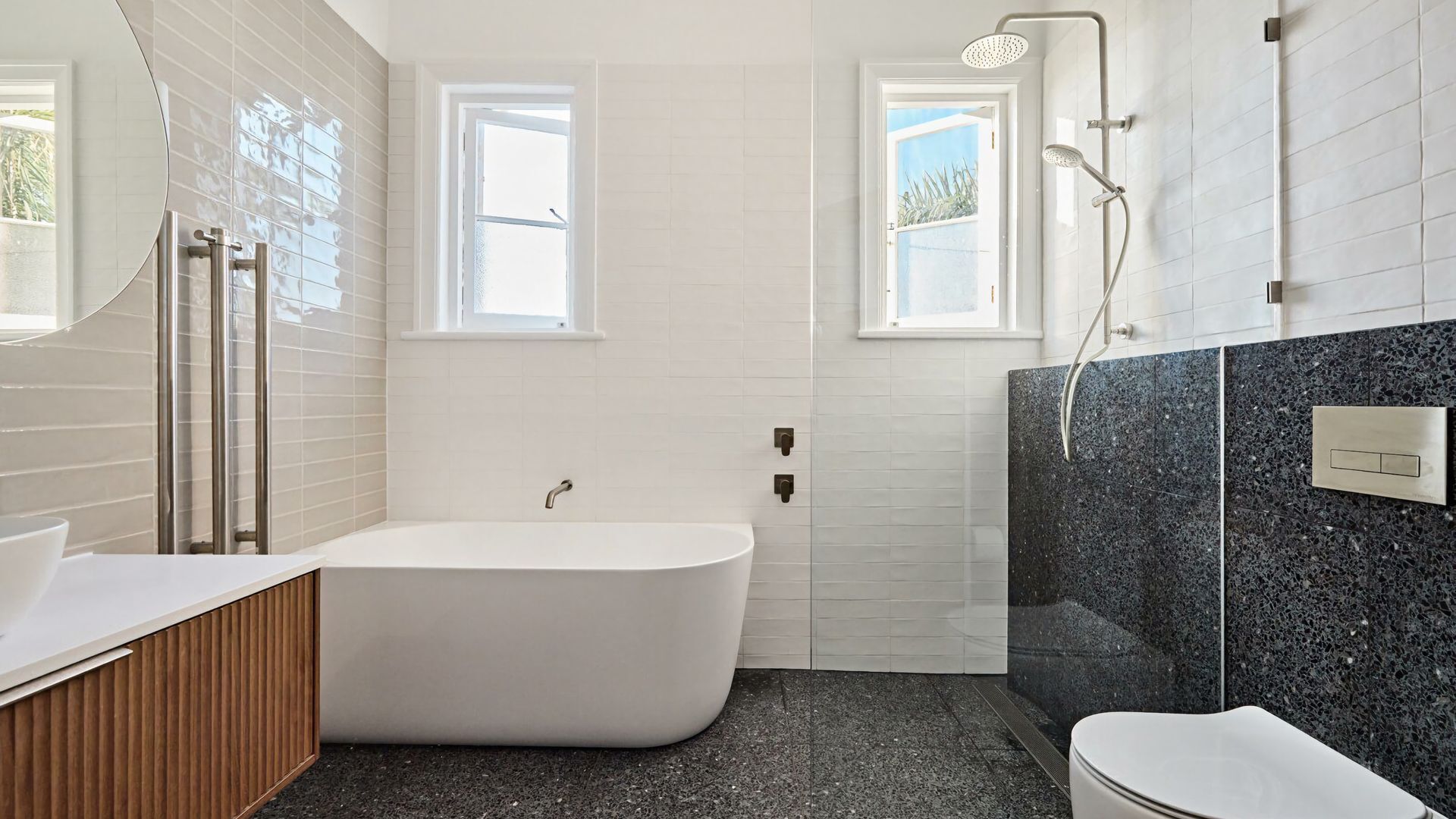 Un bagno moderno con una vasca da bagno freestanding, una doccia e un water. Due finestre assicurano luce naturale.