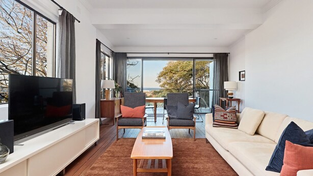 A modern living room with a flat-screen TV, a sofa, two armchairs, a coffee table, and a balcony with a view. - Coogee Treetops ISYD (Coogee)