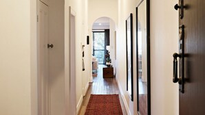 A hallway with a wooden floor, a red rug, and a view into a living area with a sofa and a table. - Coogee Treetops ISYD (Coogee)