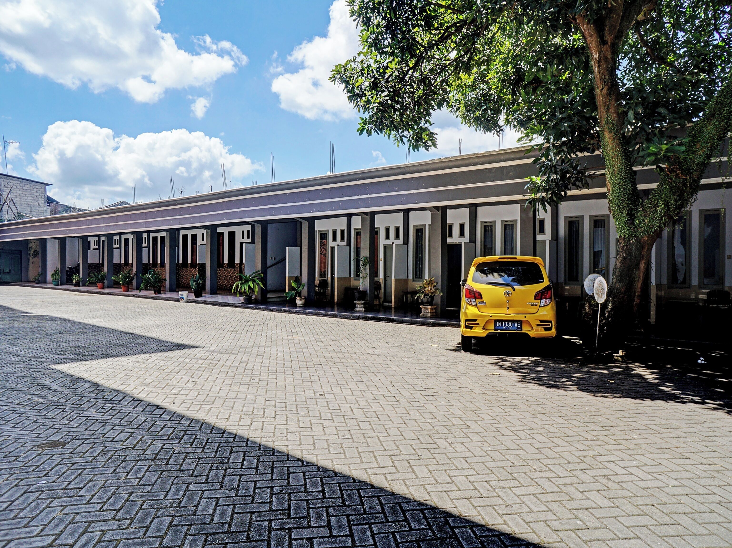 A building with a row of rooms, a paved walkway, and a yellow car parked on the side.