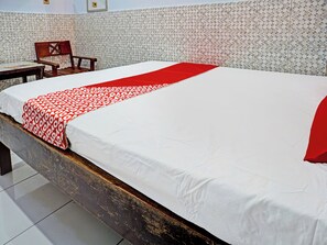 Un lit bien fait, avec une couvre-lit blanche et rouge, une tête de lit en bois et un mur orné d’un motif.