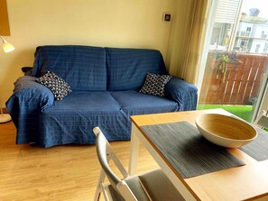 Een blauwe bank met gekleurde kussens, een houten tafel met een schaal, en een stoel.