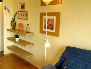 Een woonkamer met houten schappen, een vloerlamp en ingelijste kunstwerken aan de muur.