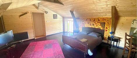 A bedroom with a bed, a TV, a red rug, and wooden walls.