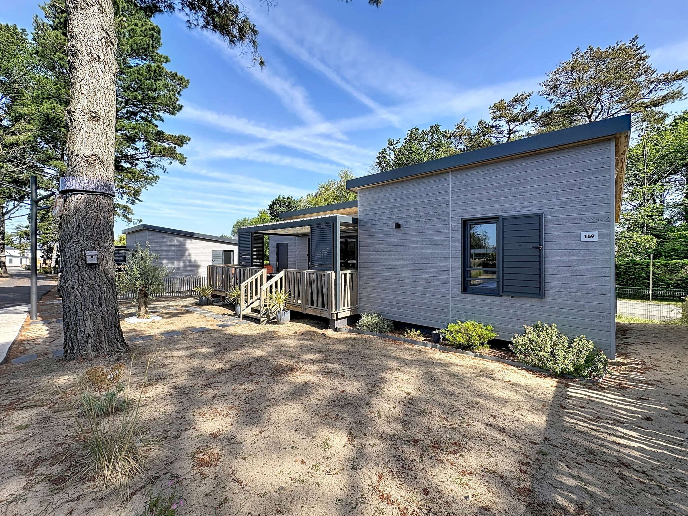 Un bâtiment moderne à deux étages, doté d’un porche abrité et d’une petite terrasse, entouré d’arbres et surplombant un ciel dégagé.