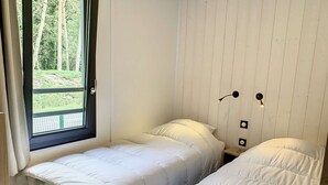 Une petite pièce avec deux lits simples, une fenêtre donnant sur un paysage verdoyant et un mur en bois.