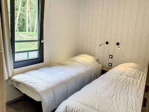 A small room with two single beds, a window with a view of a green landscape, and a wooden wall. - Charming Chalet with Heated Pool, Terrace & Parking - 6 Guests (Jullouville)