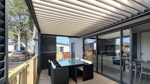 An outdoor patio with a glass-enclosed dining area, a wooden deck, and a view of the surrounding neighborhood. - Charming Chalet with Heated Pool, Terrace & Parking - 6 Guests (Jullouville)
