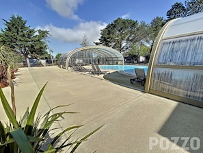 Zona de piscina con sillas de descanso y una estructura de cristal.
