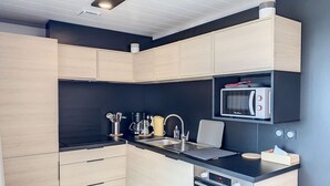 Une cuisine moderne avec des meubles de couleur bois clair, un plan de travail noir, un four encastré et un four à micro-ondes.