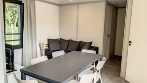 Un espace repas moderne avec une table rectangulaire, des chaises blanches et des coussins foncés.