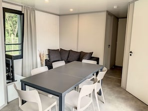 A modern dining area with a rectangular table, white chairs, and dark cushions. - Charming Chalet with Heated Pool, Terrace & Parking - 6 Guests (Jullouville)