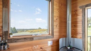 Ein Holzblockhaus-Interieur mit großem Fenster, Kamin, Esstisch und einem kleinen Hocker.