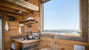 Eine Holzhütte mit einer Küche, einem großen Fenster, Holzregalen und einfachen Annehmlichkeiten.
