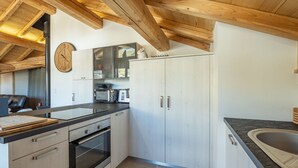 A modern kitchen with wooden beams, a built-in oven, white cabinets, and a large clock.