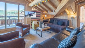 A cozy wooden interior with a leather sofa, a television mounted on the wall, and a balcony with a scenic view.