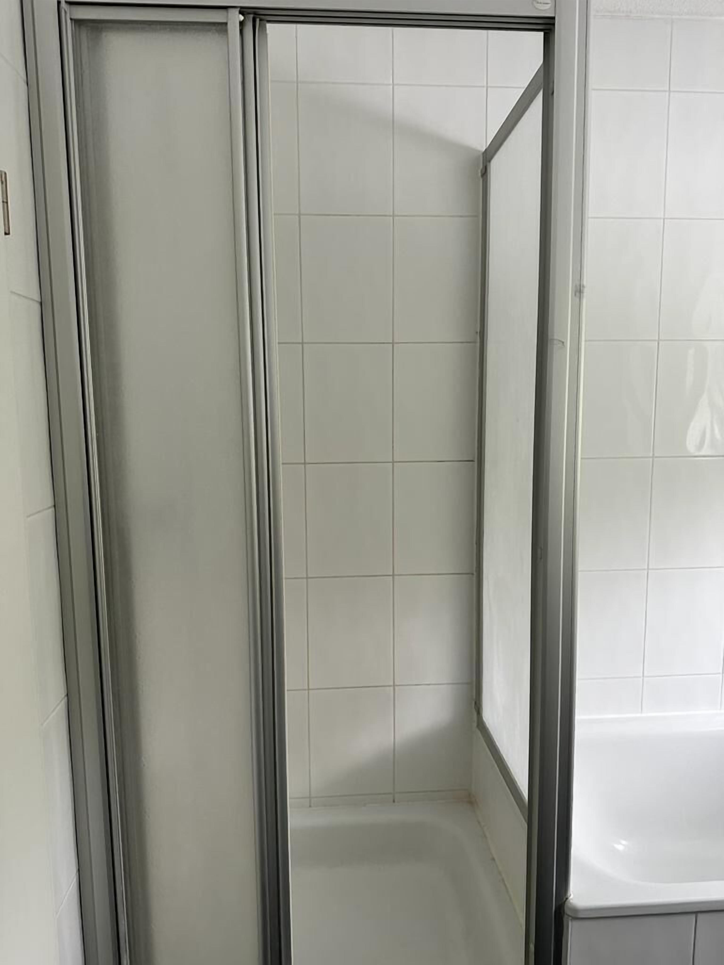 A shower area with a glass door and white tiled walls.
