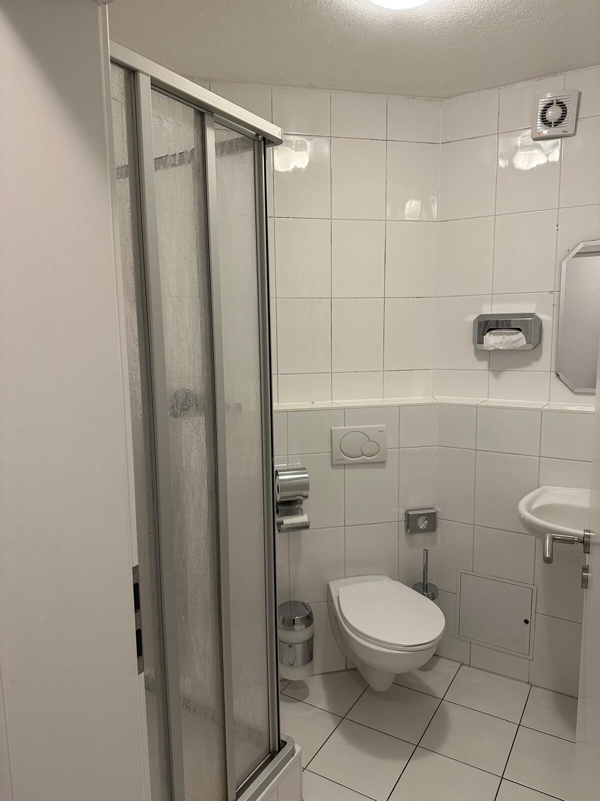 A bathroom with a glass shower door, a toilet, a sink, and a hand dryer.