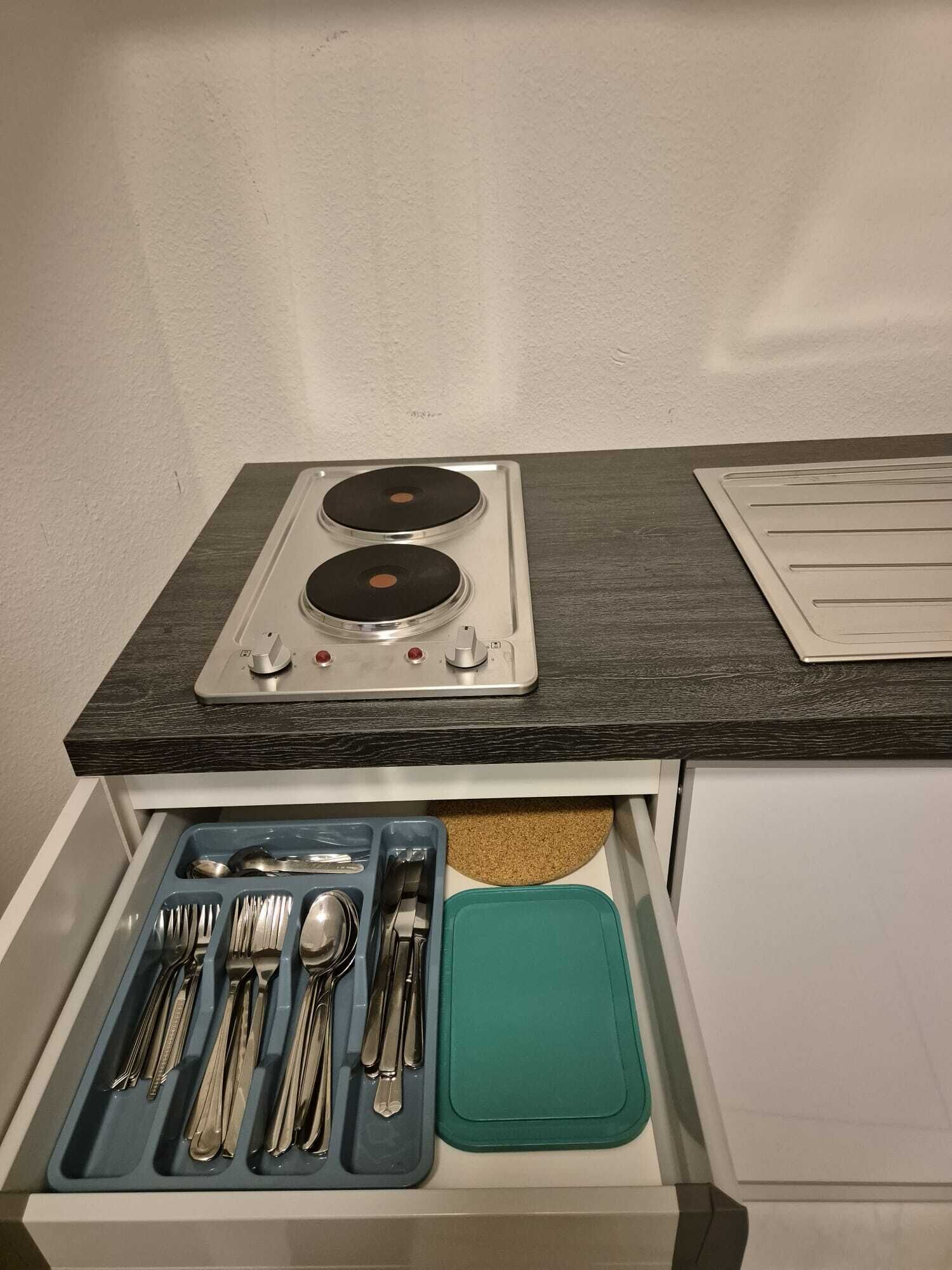 A kitchenette with a stove, two burners, and a drawer containing utensils.