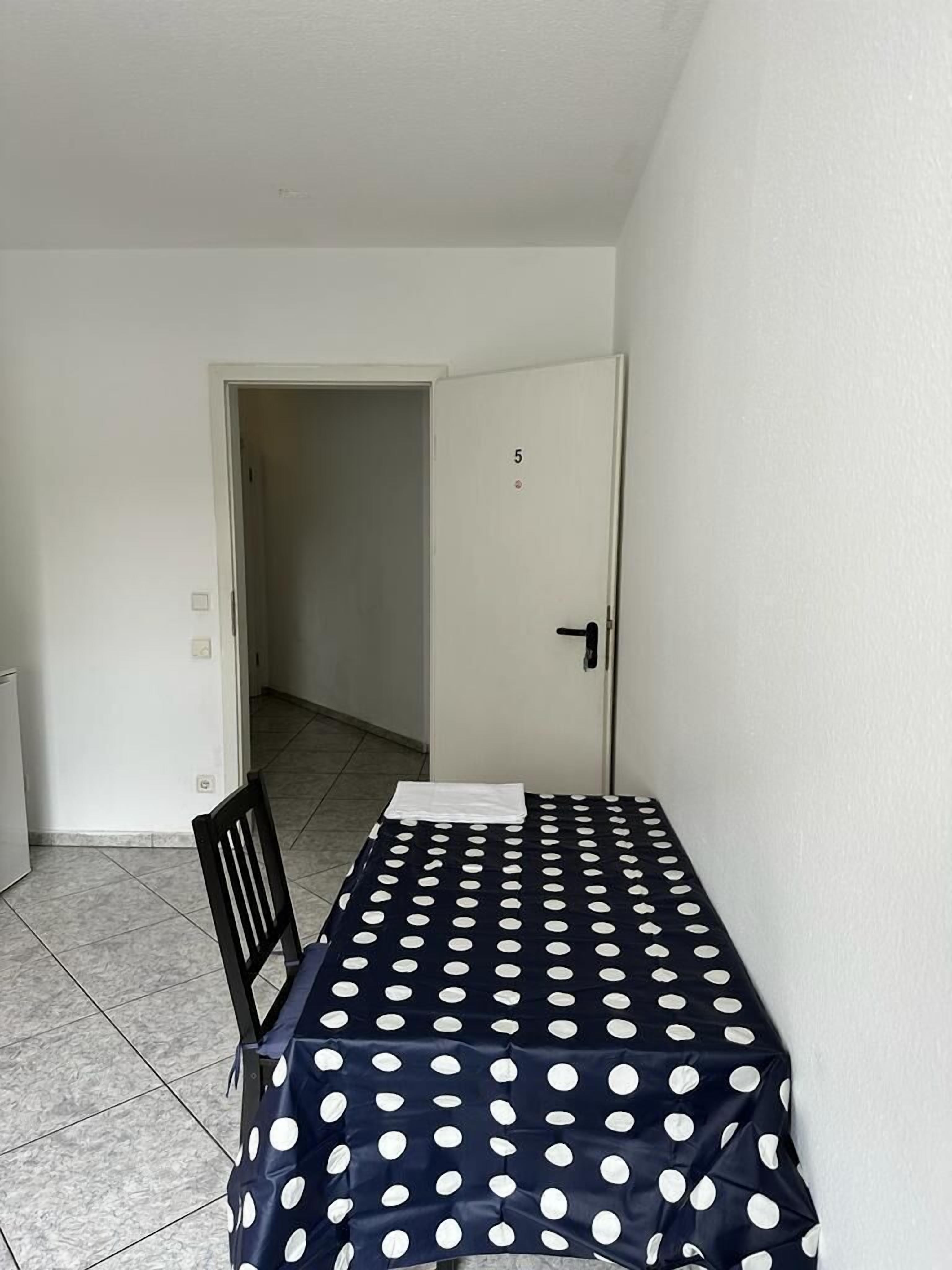 Ein kleines Zimmer mit einem Bett, einem Sessel und einer Tür mit der Nummer 5.