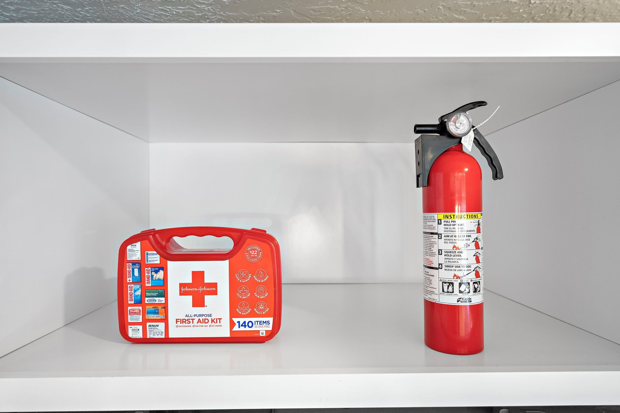 A red fire extinguisher and a red first aid kit on a white shelf.