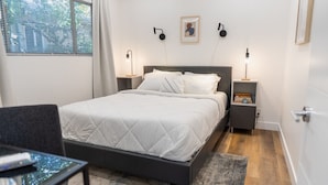 A neatly arranged bedroom with a bed, bedside tables, and a chair.
