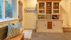 A cozy room with a wooden bench, a sign reading "DOUGLAS," and a cabinet with glass doors displaying dishes and glasses. - Your Michigan Cottage Awaits! (Douglas)