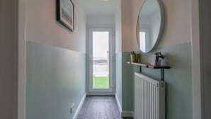 Un couloir avec une porte donnant sur l’extérieur, un radiateur, une étagère avec des plantes et un tableau encadré au mur.