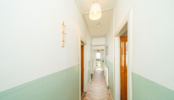 A narrow hallway with a wooden floor, white walls, and a light fixture at the end.