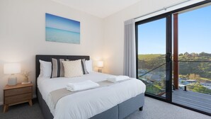 A modern hotel room with a large bed, two bedside tables with lamps, a view of a landscape through a sliding glass door. - Hilltop Haven – breathtaking ocean and mountain panoramas (Kiama)
